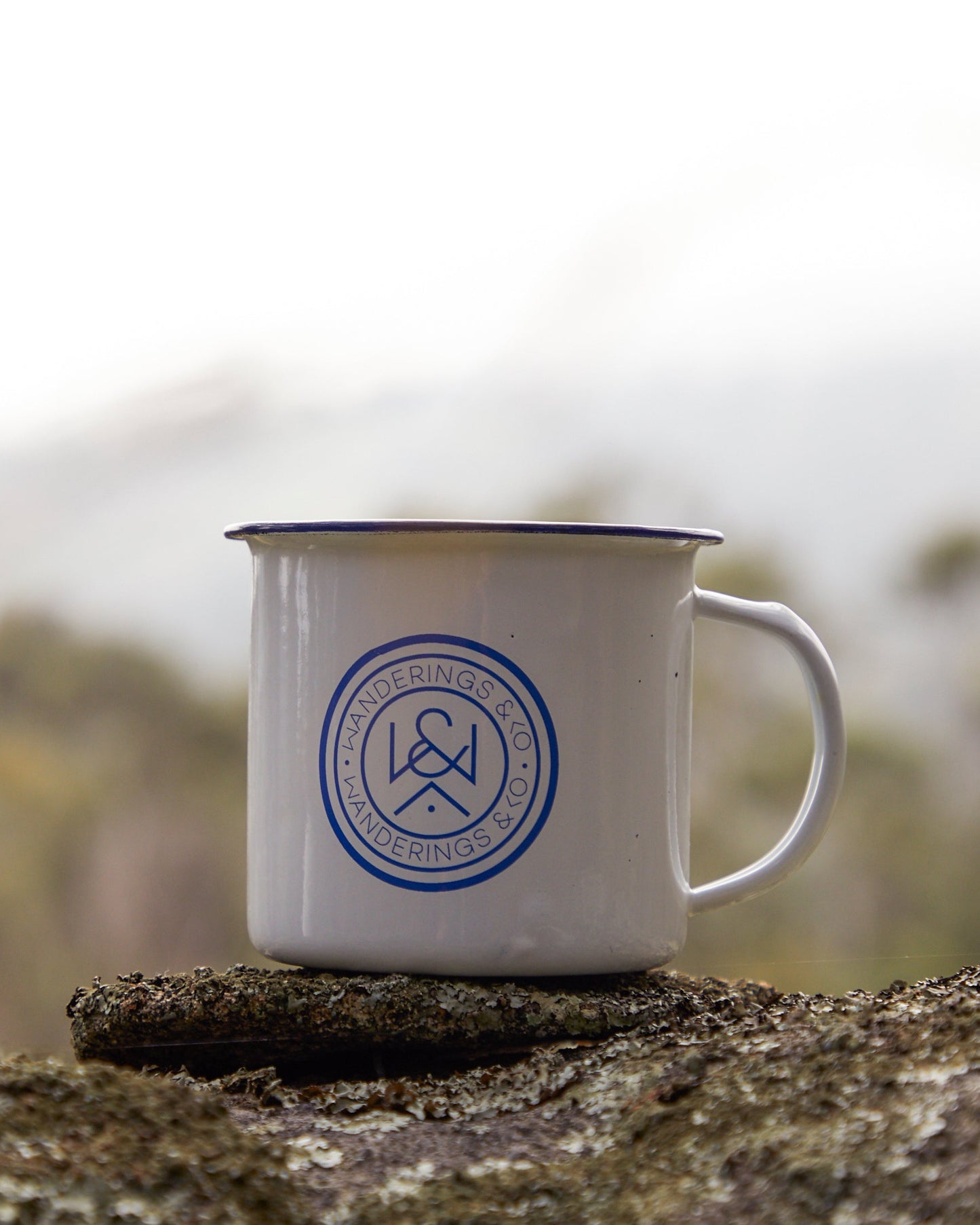 White mug with blue logo on a rock with a blurred natural background
