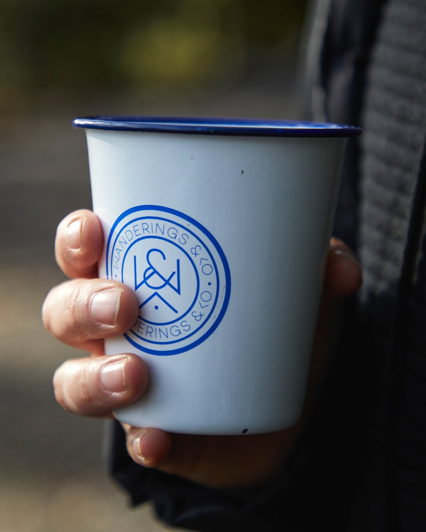 Person holding a white cup with a blue logo outdoors