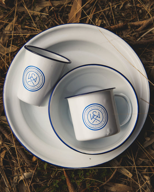 Two white cups with blue logos on a white plate on a textured brown surface